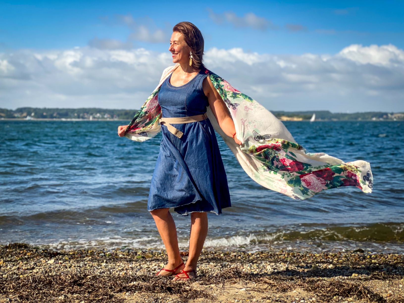 A woman standing on a windy beach with flying scarf